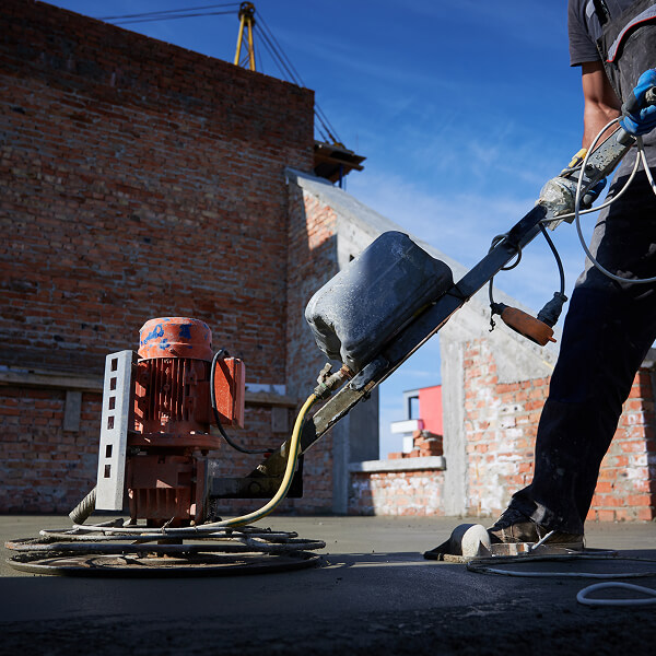 Un homme utilise une machine pour créer une surface en béton, illustrant des services complets et spécialisés.